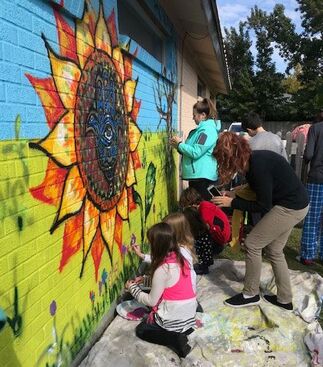 Adults and children paint mural of flower